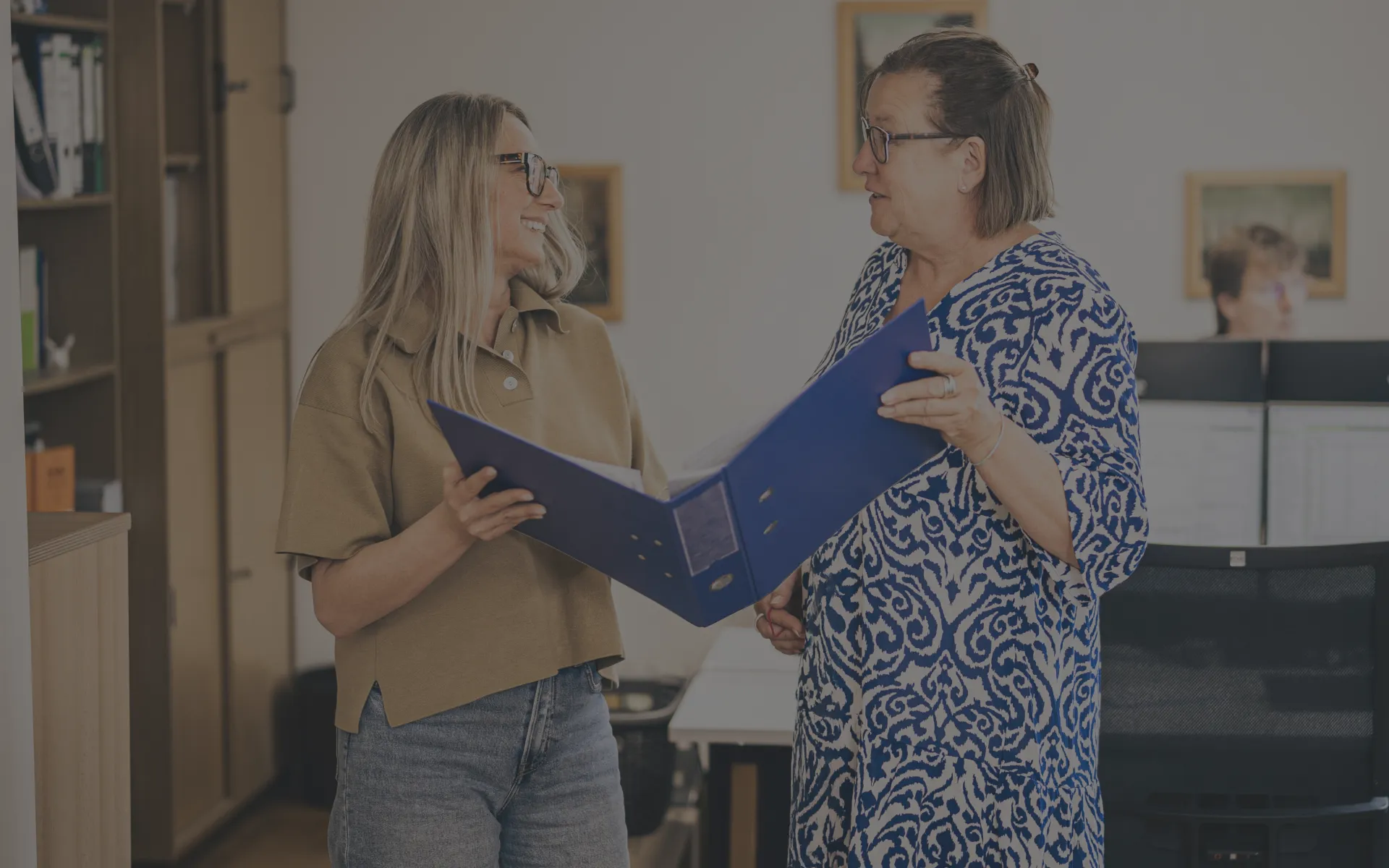 Zwei Steuerberaterinnen stehen gemeinsam mit einem Aktenordner und tauschen sich aus.