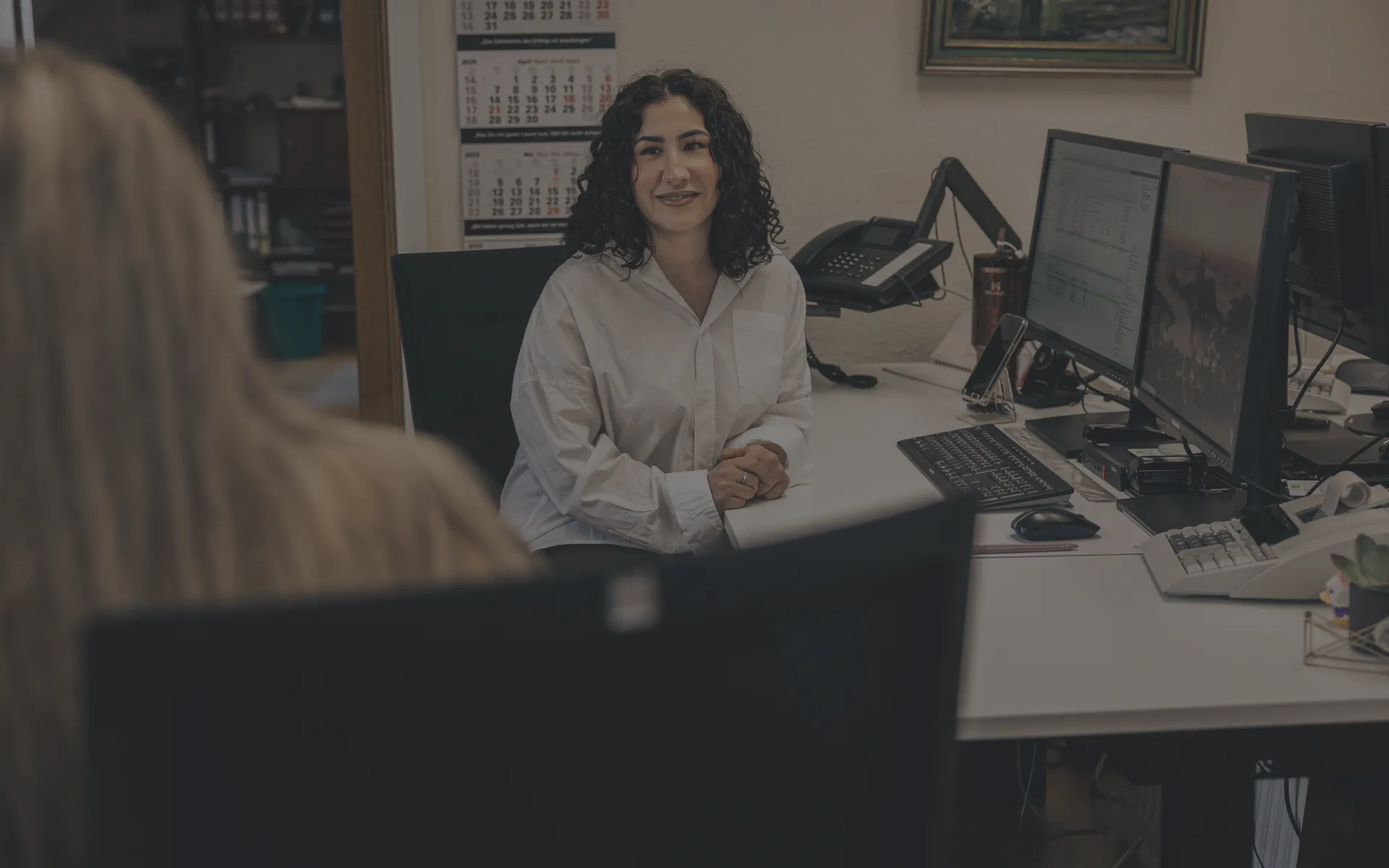 Freundliche Kollegin am Schreibtisch mit Computer und Telefon.